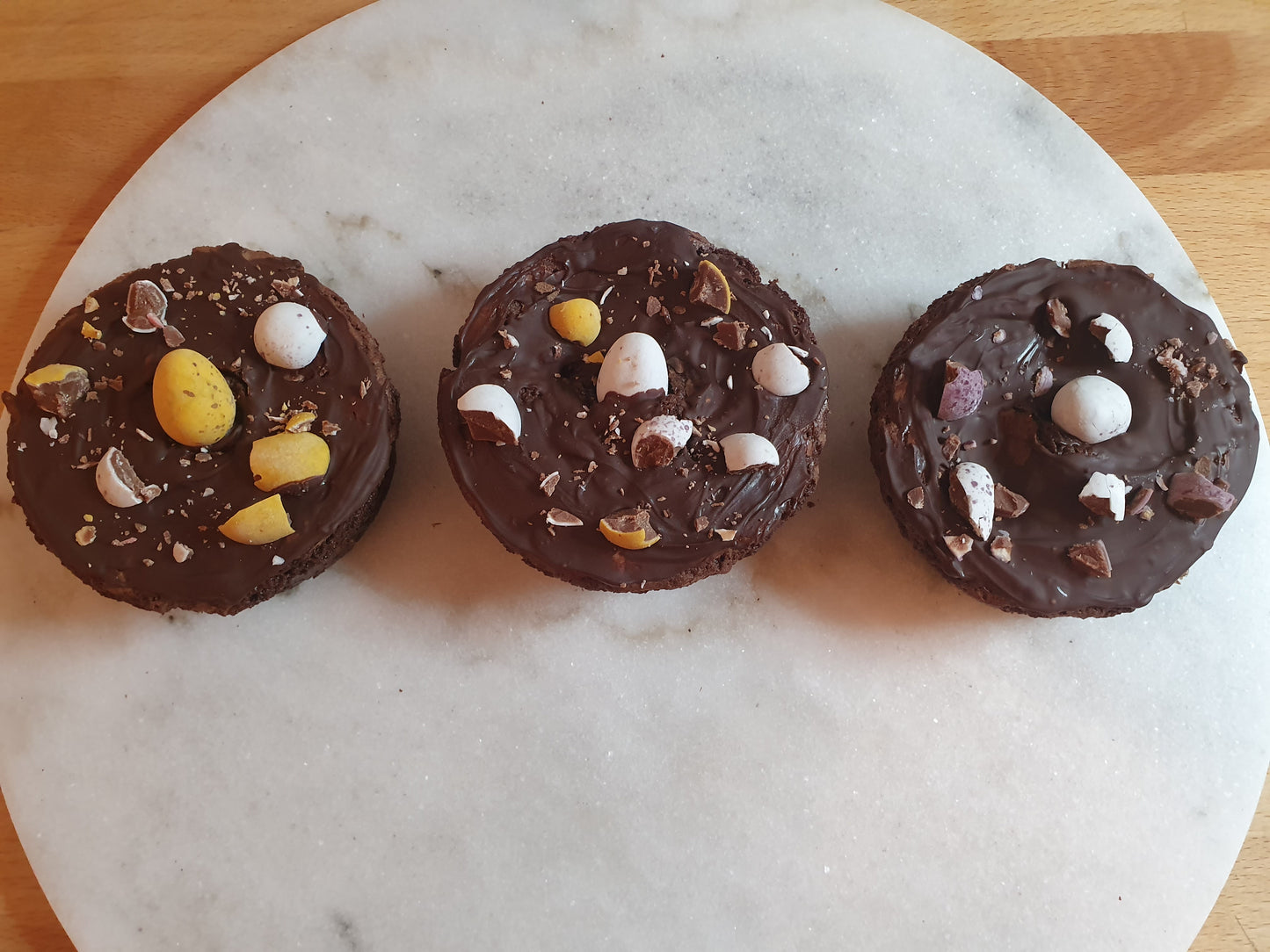 Three chocolate bronuts decorated with dark chocolate and Mini Eggs