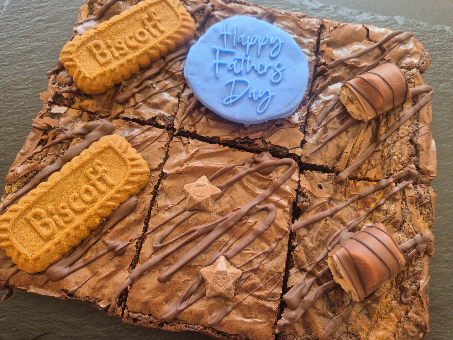 Six chocolate brownies topped with Biscoff biscuits and kinder bueno chocolate bar pieces. Includes a blue fondant topper which says Happy Father's Day