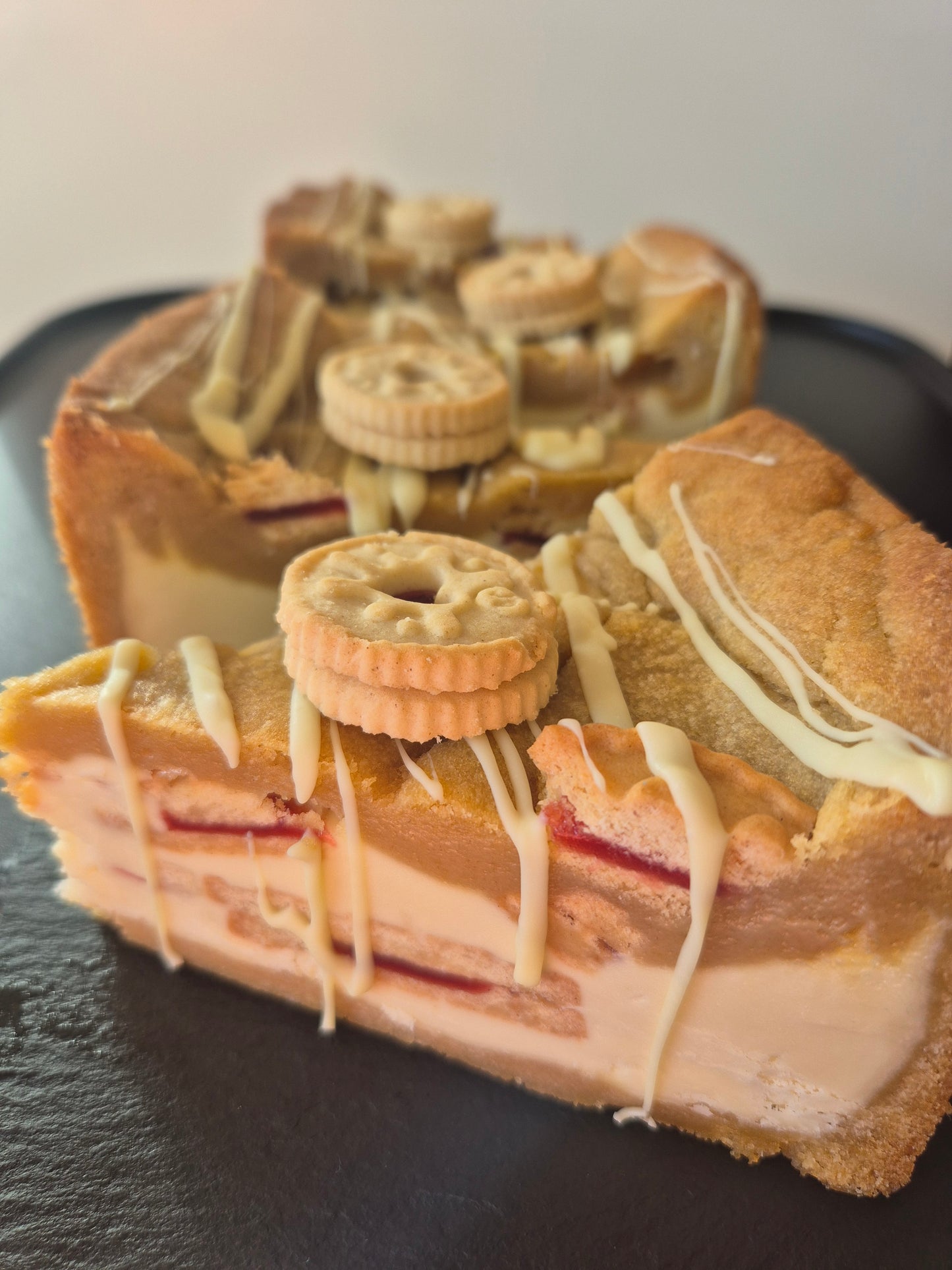 4 jammie dodger cookie pie slices on a dark background. Each cookie pie slice is topped with white chocolate drizzle and mini jammie dodger biscuit