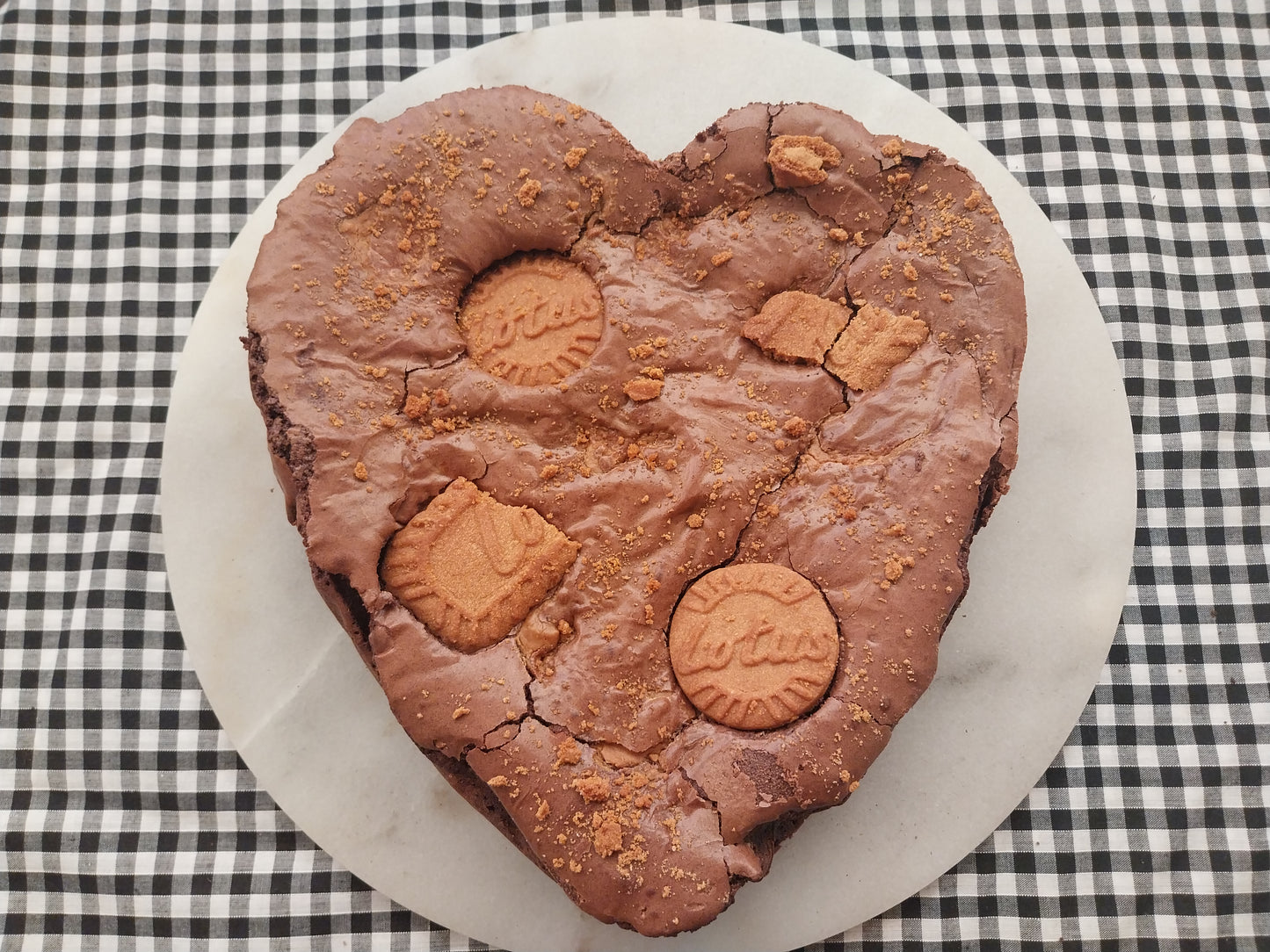 A large heart shaped brownie on a marble slate. The heart shaped brownie i s decorated with Biscoff biscuits.