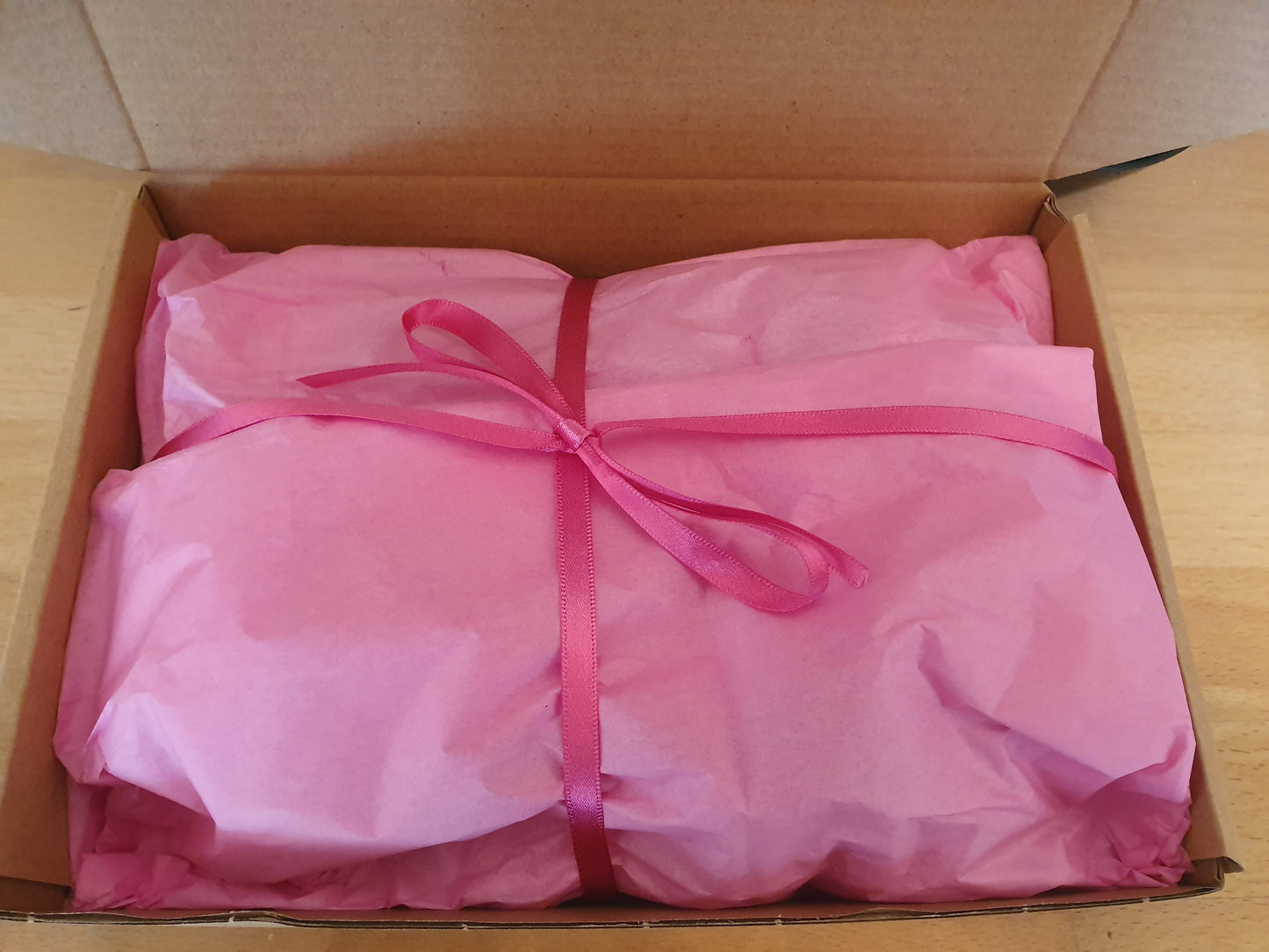 Brownies (not visible) packaged in a cardboard box wrapped in pink tissue paper and with a pink ribbon bow