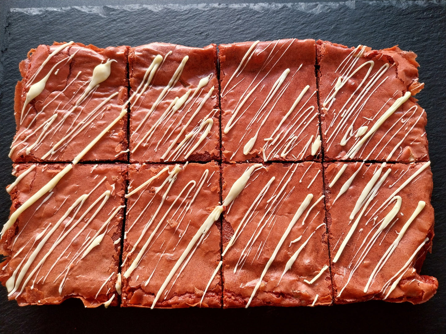Eight red velvet brownies drizzled with white chocolate