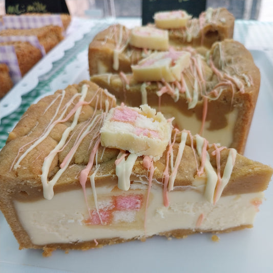 4 slices of Battenberg cookie pie on a tray. Filled with white chocolate spread and pieces of Battenberg cake and decorated with white and pink chocolate drizzle and a small slice of Battenberg cake on top.