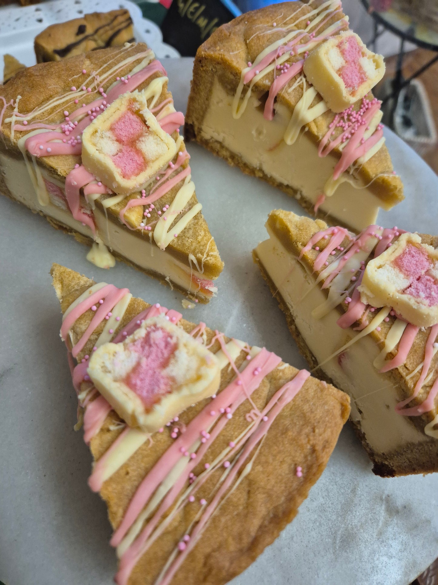 4 slices of battenberg cookie pie slices decorated with white chocolate drizzle and battenberg cake piece on top placed on a cake stand