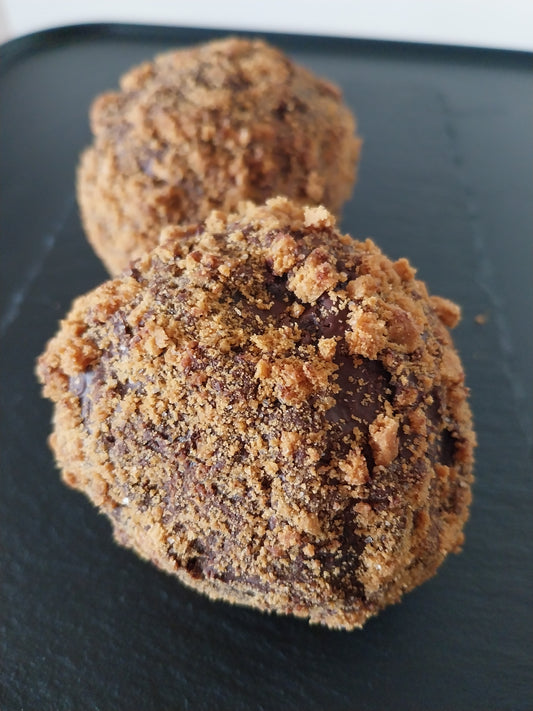 Close-up of two chocolate brownie scotch eggs coated in Biscoff crumb on a dark surface