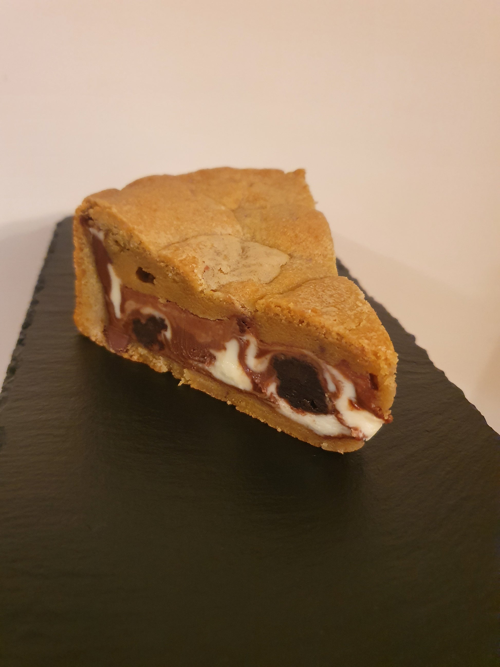 Slice of cookie pie filled with chocolate filling and chunks of brownie on a slate