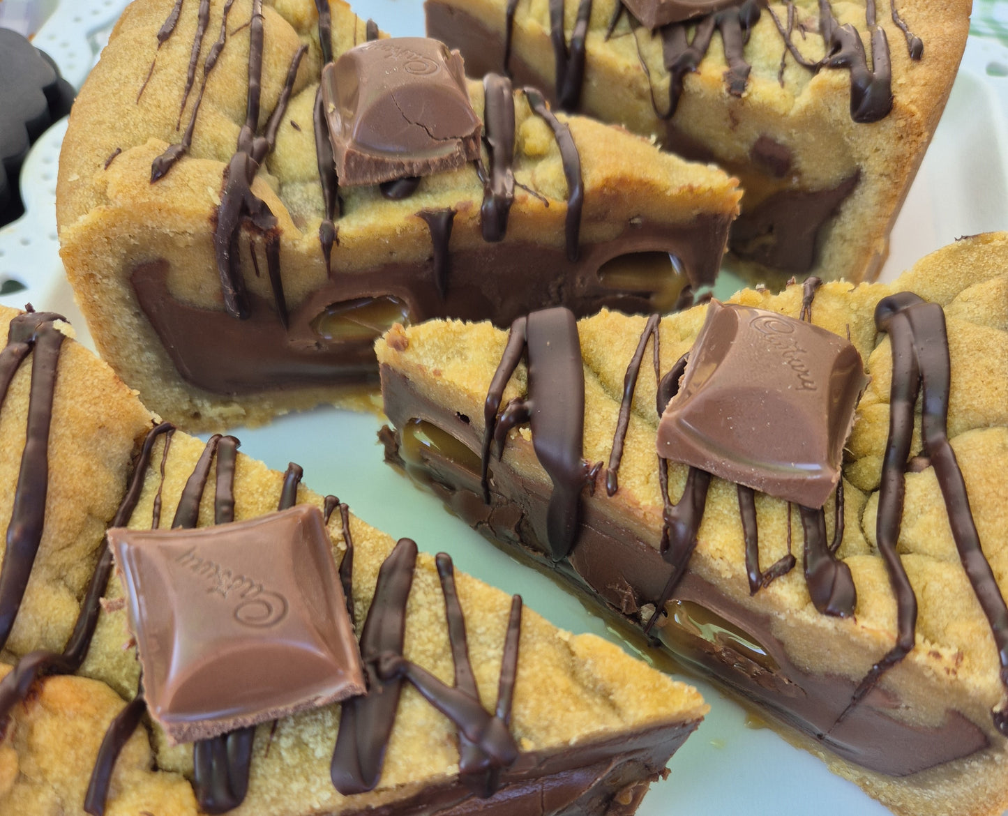 Cadbury caramel chocolate cookie pie slices with chocolate drizzle and Cadbury Caramel pieces on a white plate