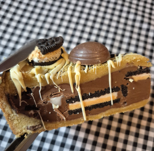 Close-up of a slice of creme egg oreo cookie pie with chocolate and cookie layers on a checkered background