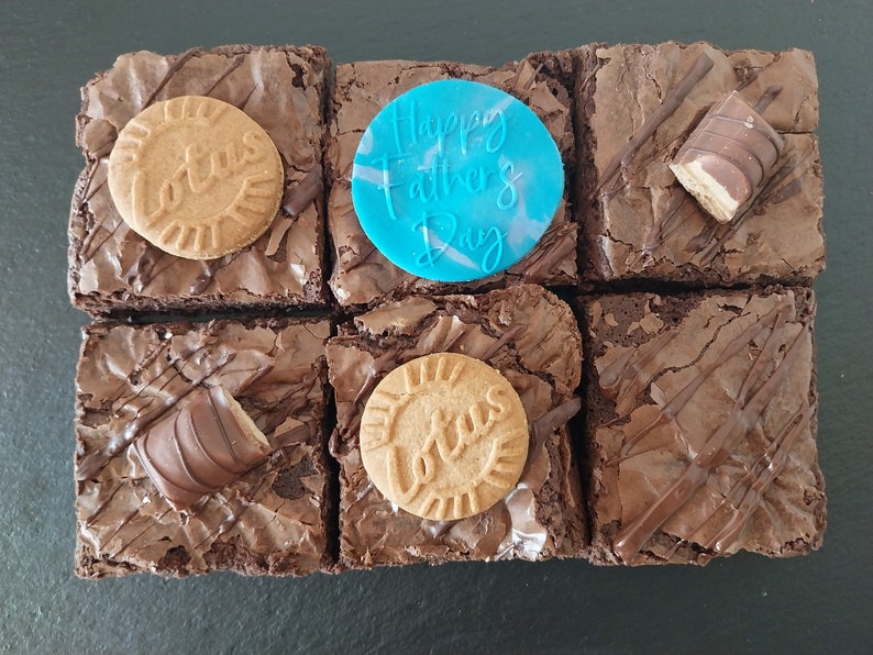 Six chocolate brownies topped with Biscoff biscuits and kinder bueno chocolate bar pieces. Includes a blue fondant topper which says Happy Father's Day