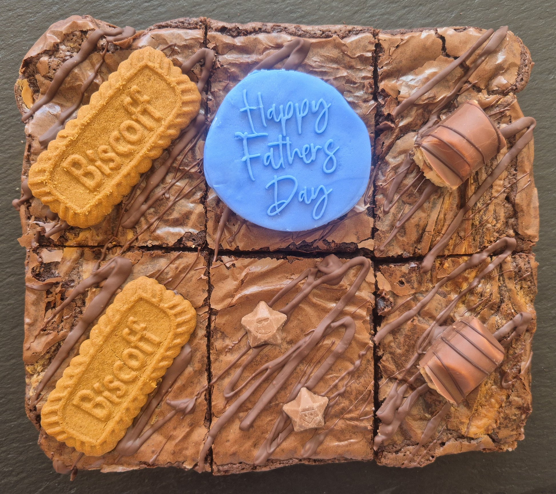Six chocolate brownies topped with Biscoff biscuits and kinder bueno chocolate bar pieces. Includes a blue fondant topper which says Happy Father's Day
