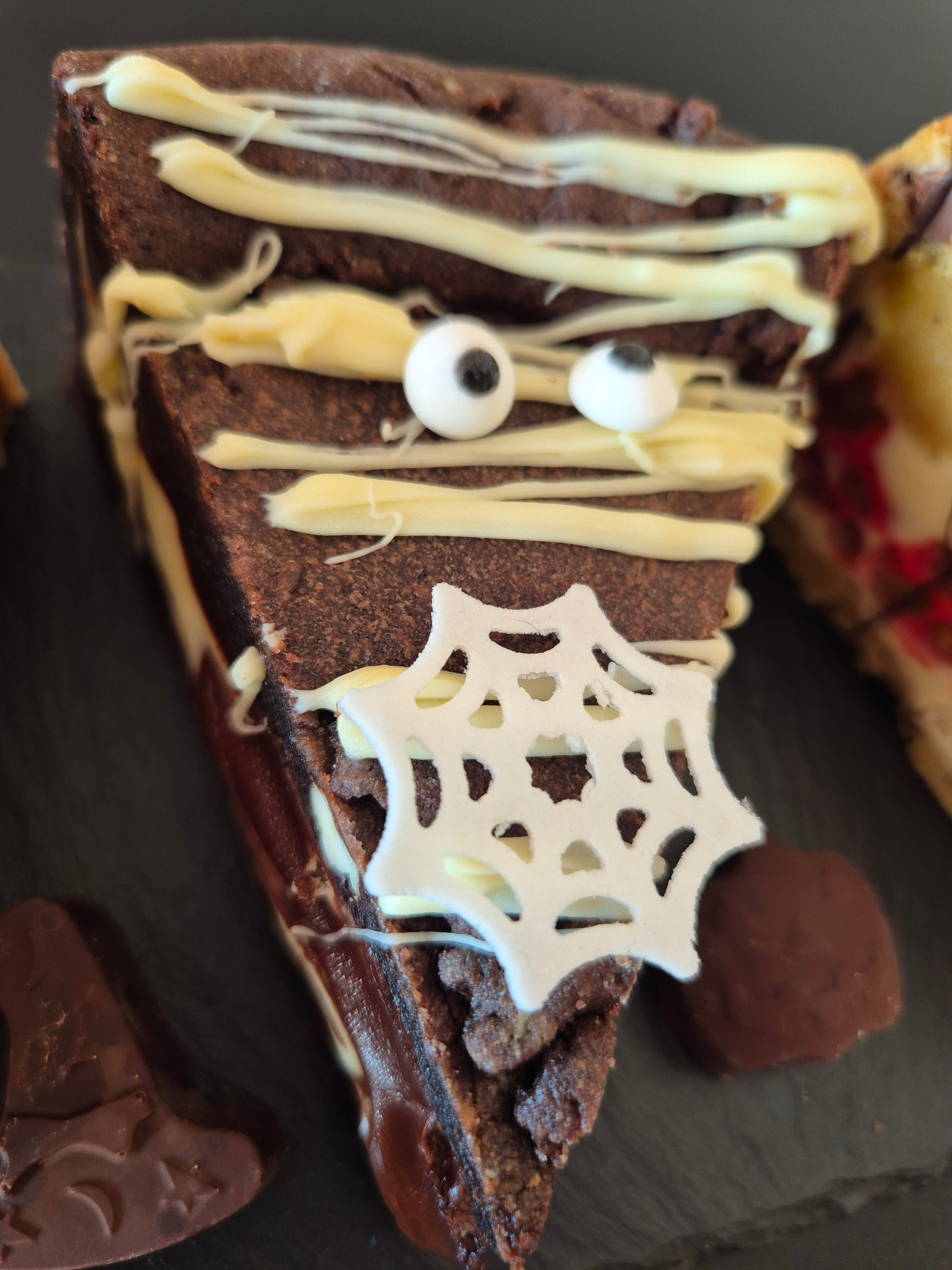 Halloween-themed chocolate cookie pie with spider web and eyeball decorations on a dark surface.