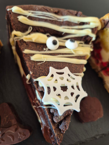 Halloween-themed chocolate cookie pie with spider web and eyeball decorations on a dark surface.