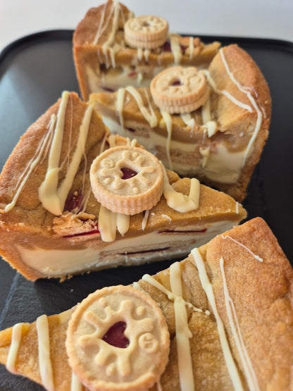 4 jammie dodger cookie pie slices on a dark background. Each cookie pie slice is topped with white chocolate drizzle and mini jammie dodger biscuit