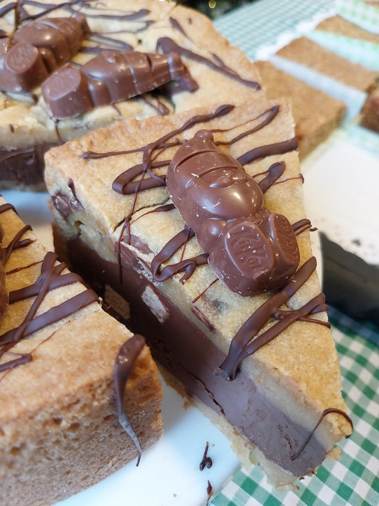 A slice of cookie pie filled with milk chocolate and Kit Kat pieces, drizzled with dark chocolate and Kit Kat Santa