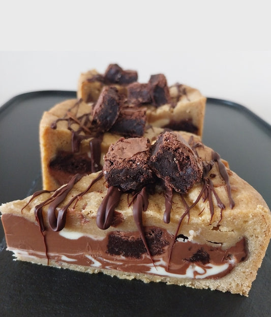 Four slices of cookie pie filled with milk and white chocolate, brownie chunks and topped with chocolate drizzle and brownie pieces