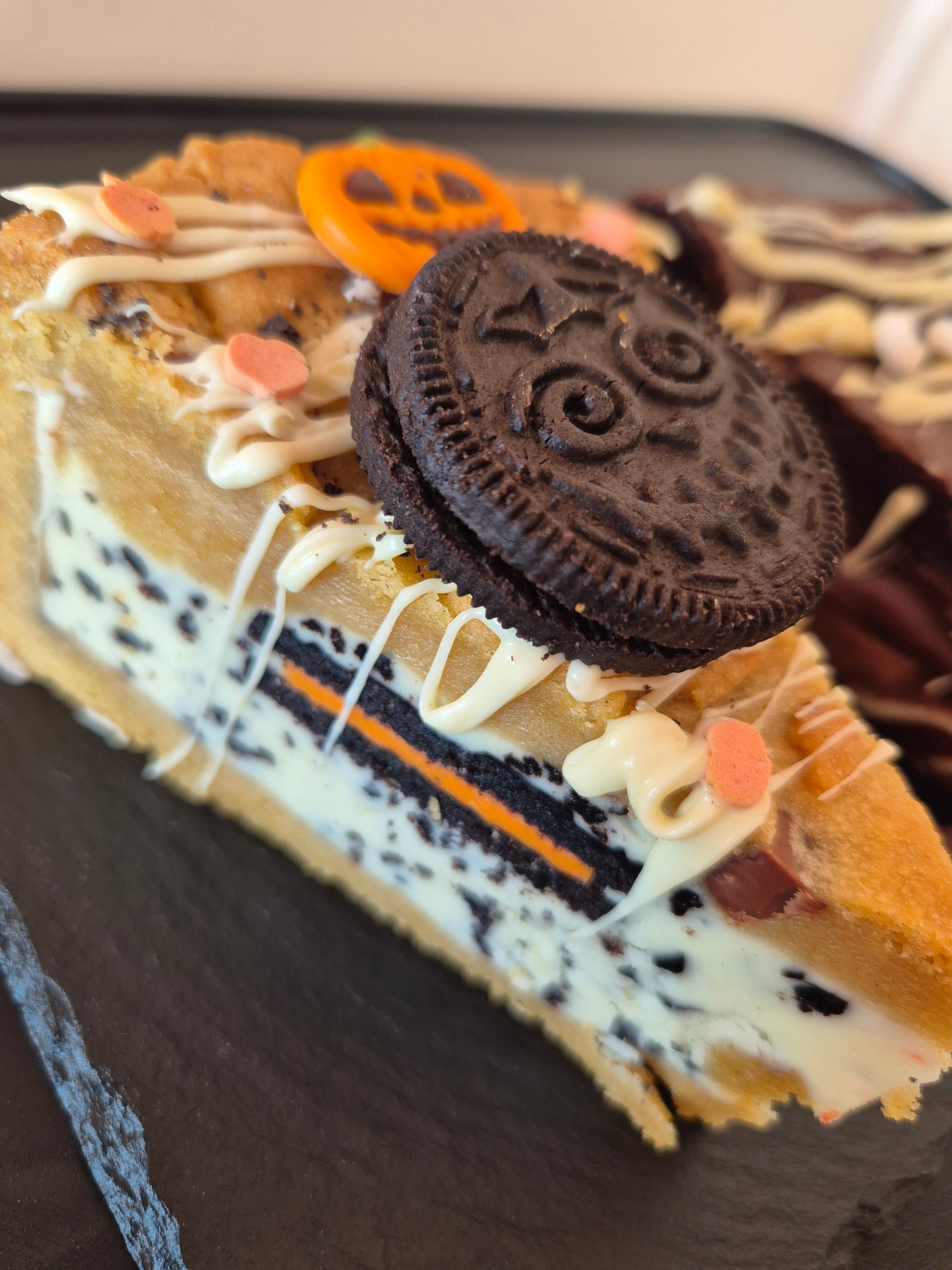 Close-up of a cookie pie slice with Oreo cookie, chocolate, and white chocolate on a dark surface