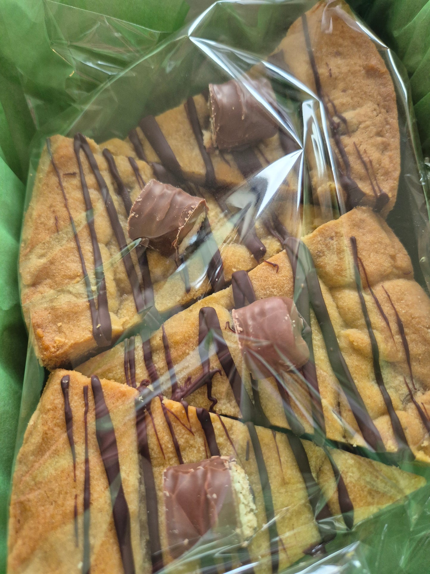 Packaged twix cookie pie slices with chocolate drizzle on green tissue paper