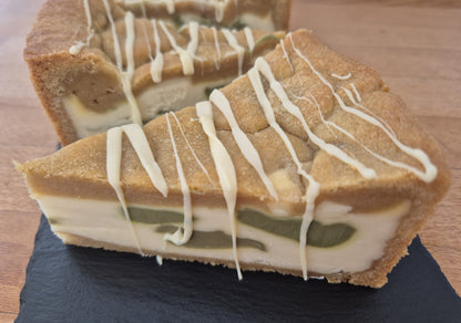 White chocolate and pistachio cookie pie decorated with white chocolate drizzle on a dark slate
