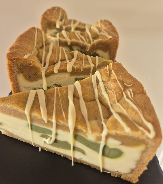 White chocolate and pistachio cookie pie decorated with white chocolate drizzle on a dark slate