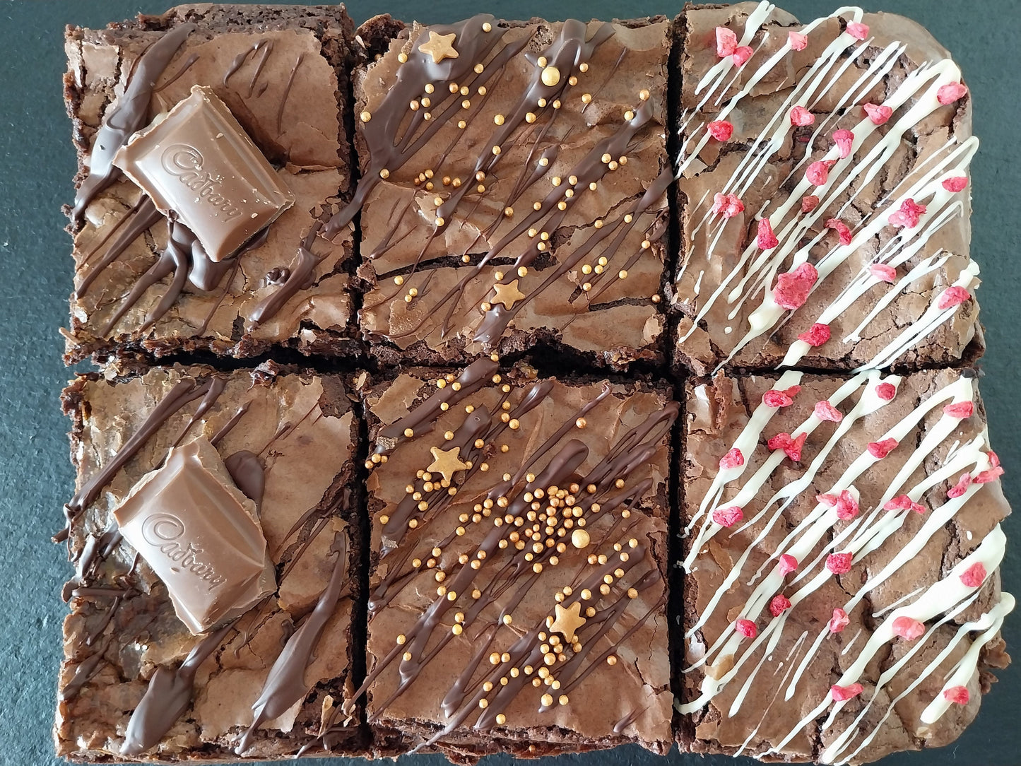 Six brownies on a slate two are chocolate caramel, two are classic chocolate and two are white chocolate raspberry