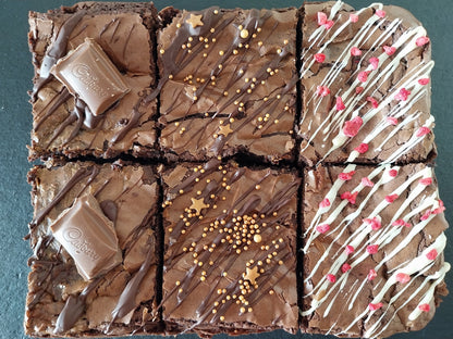 Six brownies on a slate two are chocolate caramel, two are classic chocolate and two are white chocolate raspberry