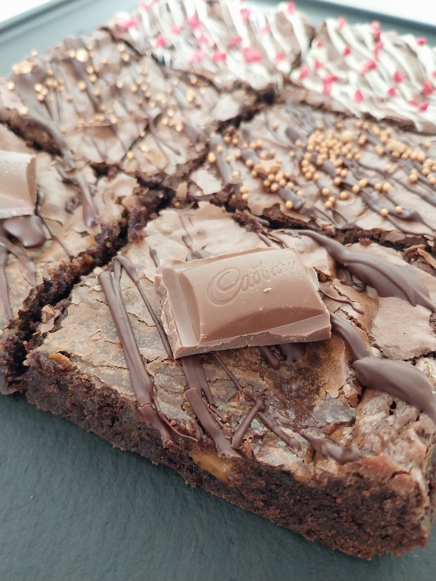 Side view of six brownies on a slate two are chocolate caramel, two are classic chocolate and two are white chocolate raspberry