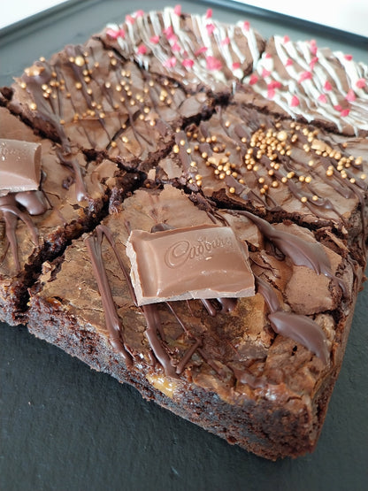 Side view of six brownies on a slate two are chocolate caramel, two are classic chocolate and two are white chocolate raspberry