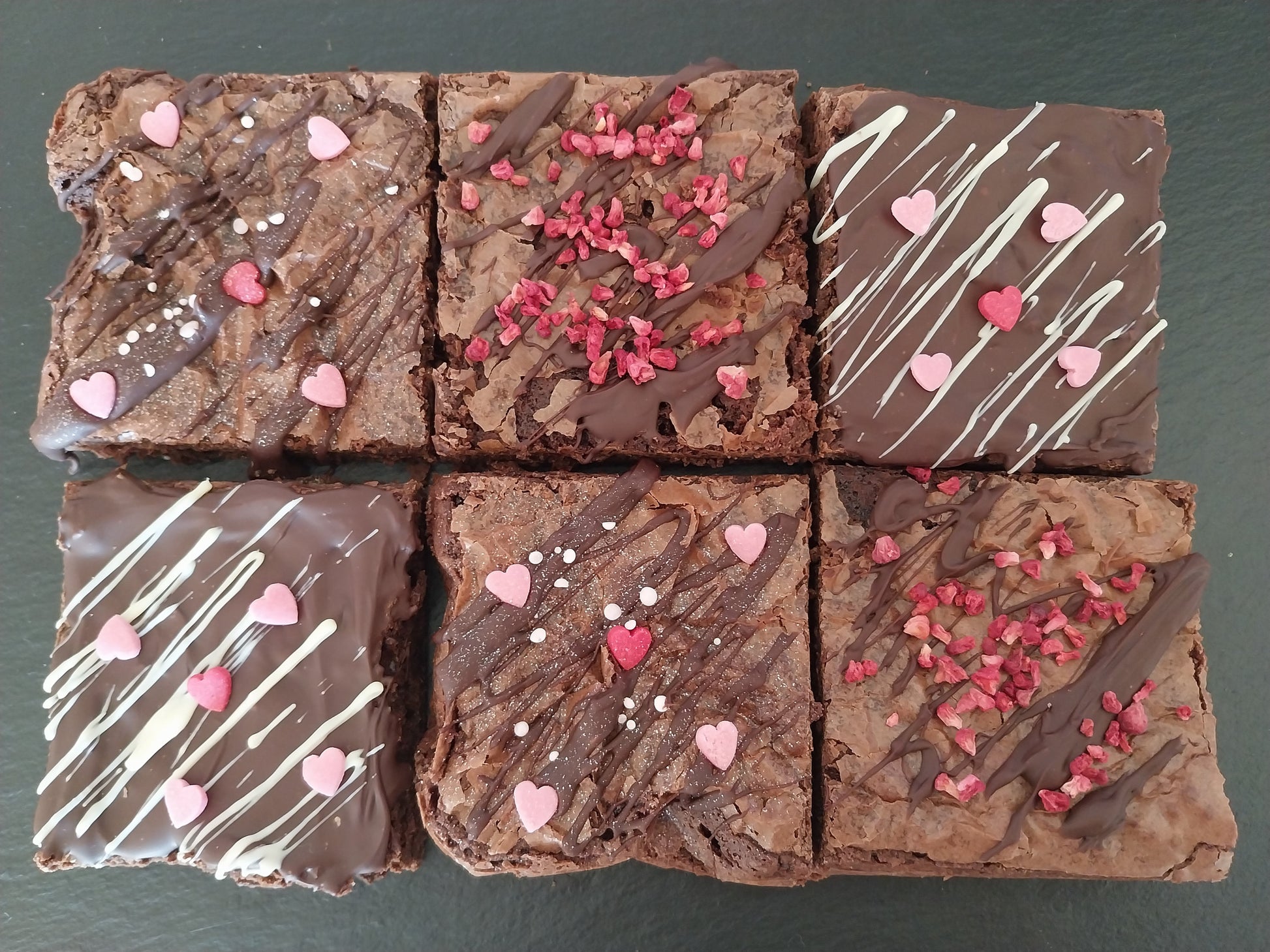 Six Valentines chocolate brownies decorated with chocolate drizzle, heart and pink sprinkles and raspberry pieces